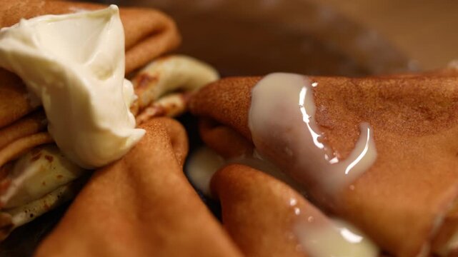 This appetizing close-up shot captures a rustic serving of golden-brown thin pancakes, likely blini or crepes, folded into triangular shapes. 
