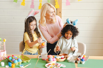 Grandmother, girl, and boy painting Easter eggs together, celebrating holiday
