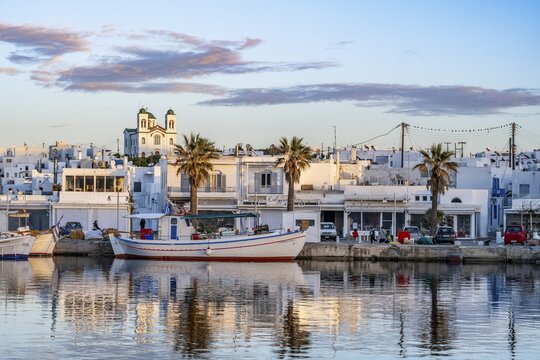 View of Naoussa, Fishing boats in the harbour at sunset, reflected in the sea, White Cycladic houses and church Agios Faneromeni, Naoussa, Paros, Cyclades, Greece