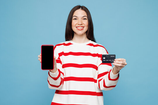 Young woman wears red striped sweatshirt casual clothes using blank screen area mobile cell phone hold credit bank card shopping online order delivery booking tour isolated on plain blue background.