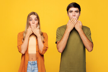 Naklejka premium Young shocked sad surprised couple two friends family man woman wear casual clothes cover mouth with hand look camera together isolated on pastel plain light yellow color background studio portrait