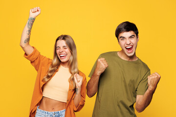 Young couple two friends family man woman wear casual clothes looking camera together do winner gesture celebrate clenching fists say yes isolated on pastel plain light yellow color background studio.