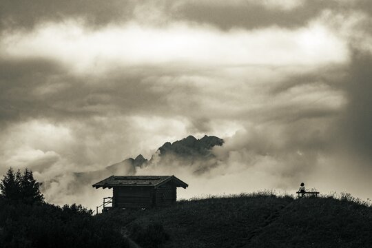 Mountain hut with bench and climber and dramatic clouds in the background, Bach, Lechtal, Tyrol, Austria