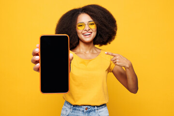 Naklejka premium Young woman of African American ethnicity wear t-shirt casual clothes hold use point on mobile cell phone with blank screen workspace area isolated on plain yellow orange background Lifestyle concept