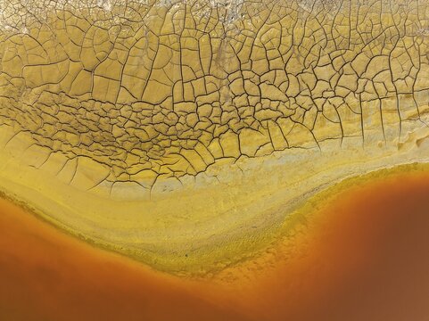 Cracked earth at the bank of the Rio Tinto (Red river) with its deep reddish hue due to oxidised iron minerals in its water, aerial view, drone shot, Huelva province, Andalusia, Spain