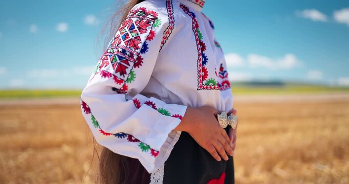 Bulgarian girl wearing traditional ethnic bulgarian costume with color embroideries and ancient folk belt buckle standing on a golden wheat field during wheat harvest, Bulgaria