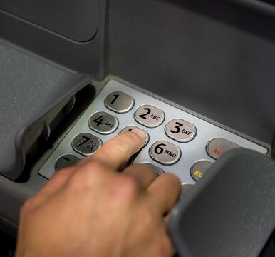 Hand at an ATM, entering the PIN, withdrawing money