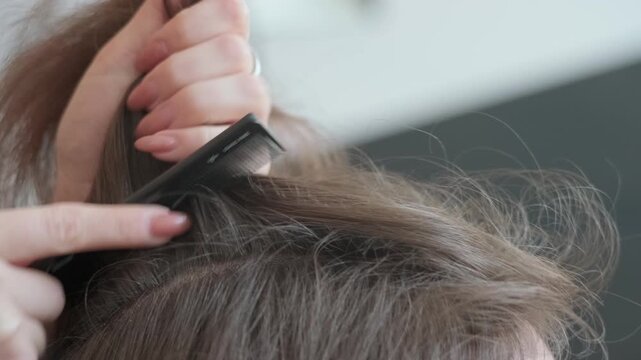 Extreme close up of a stylist's hand with a ring sectioning hair for an extension procedure