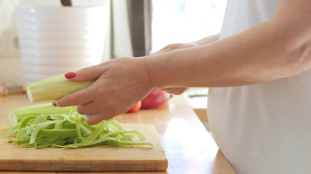 Woman is cutting celery on a cutting board. She is wearing a white shirt. There are several other vegetables on the cutting board, including a pepper and a carrot