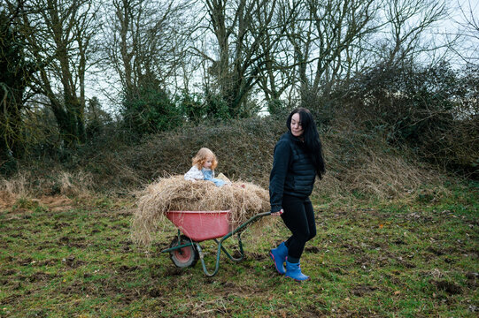 Mother wheeling daughter in a wheelbarrow full of hay in a field in Ireland