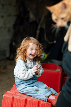 The joy of a toddler girl about to hold her ginger cat on her lap