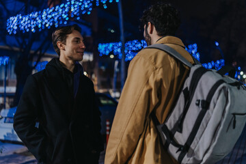 Fototapeta premium Two men converse on a city street at night beneath blue festive lights, creating an urban, friendly mood.