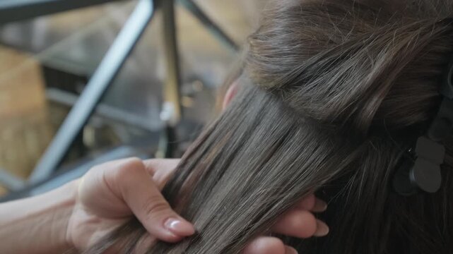 Professional hair stylist hands meticulously parting sections of dark hair with a clip during an extension procedure
