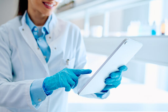 Female scientist wearing lab coat and blue gloves, interacting with a tablet computer during experimental data analysis in a modern facility