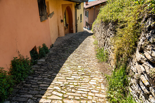 sunny stone path seen from above descends between a low stone wall on the right and pink-coloured houses on the left
