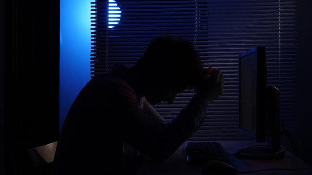 Frustrated man silhouette slamming keyboard at night, expressing burnout, anger and stress from long overtime hours at a dark office desk, overwhelmed and exhausted