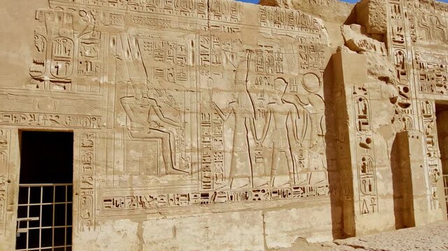 Closeup of ancient Egyptian hieroglyphic inscriptions with cartouches and bird symbols carved in sandstone wall at Medinet Habu temple in Luxor Egypt, detailed royal text.