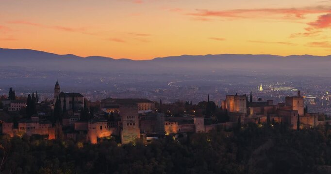 zoom in time lapse of aerial view of Alhambra at sunset with lighting on and mountain, Granada, Spain