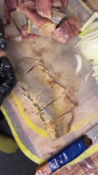 Vertical video: people prepare herring on a board, handling pieces with gloves and checking for bones.