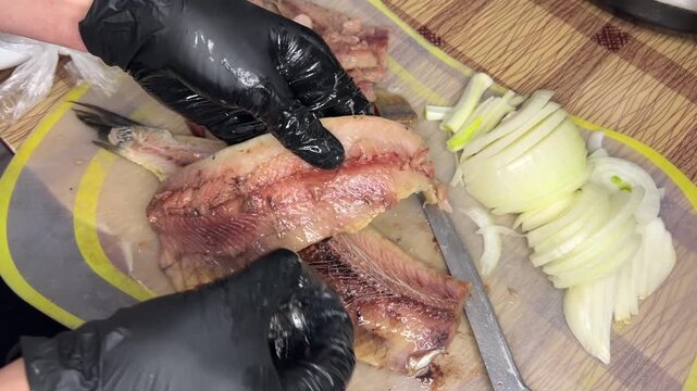Woman in gloves cleaning herring from bones on plastic board