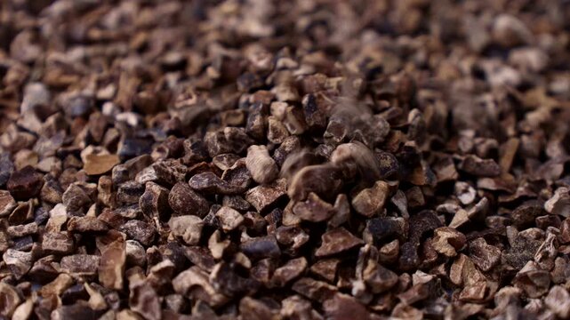 Roasted brown crushed cocoa nibs falling down close up