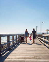 Fototapeta premium Family Vacation: Walking with Baby Stroller on Sunlit Beach Pier - Summer Travel Adventure