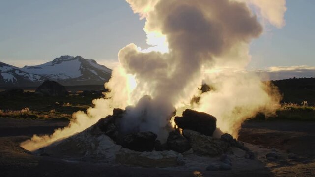 Smoke billows from a geothermal vent in a mountainous landscape at sunrise