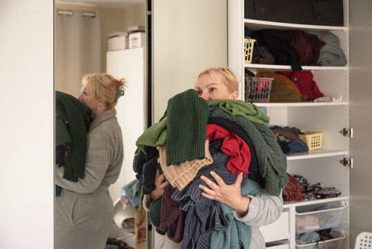Woman holding a large pile of sweaters and knitwear