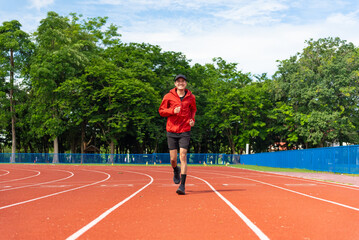 Fototapeta premium Young Asian men are exercising with outdoor running with a running track background in the morning. Concept healthy running and outdoor exercise, Tracking shot,