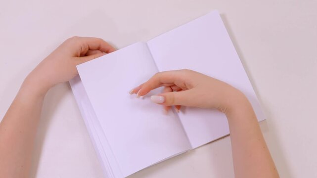 Person is holding a book open to a blank page. The book is white and the person's hands are on the pages