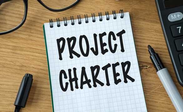 PROJECT CHARTER text written in a notebook on a wooden desk with a black marker for business project initiation and management concept.