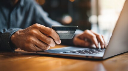 An individual is using a laptop computer while holding a credit card to make purchases through online shopping