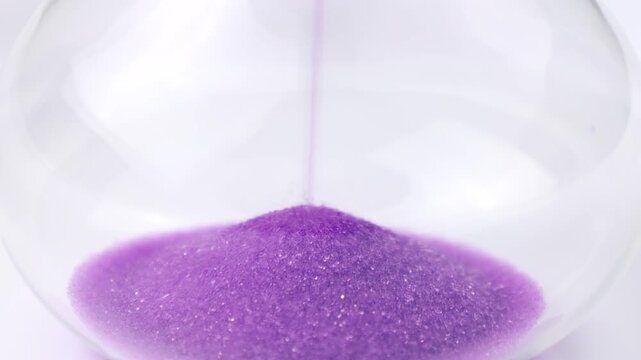 Transparent hourglass with flowing purple sand on white background. Old classic timer. Time concept