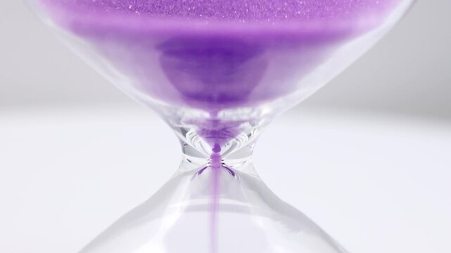 Transparent hourglass with flowing purple sand on white background. Old classic timer. Time concept