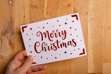 Christmas card with Merry Christmas message, stars, and red accents held in a hand against a wooden backdrop. Perfect fo © vegefox.com