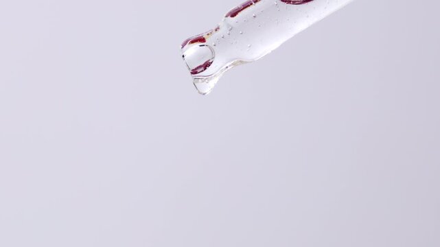 Cosmetics transparent liquid gel dripping from glass pipette on white background