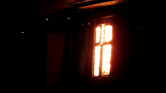 The window of the house is on fire, the night flame of the disaster. The natural wild flame is burning the building from the inside.