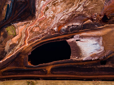Aerial view of the stark contrast between the dark waters and the red earth, creating an otherworldly landscape, Aluminium Refinery, Western Australia, Australia.