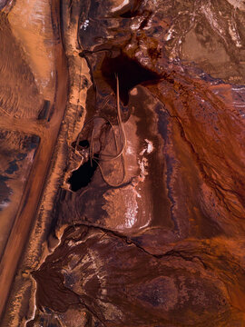 Aerial view of the rusty earth is carved with deep, dark fissures near the Aluminium Refinery, contrasting sharply with the pale, winding roads, Aluminium Refinery, Western Australia, Australia.
