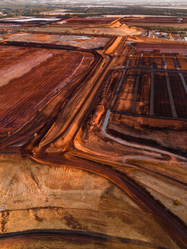 Aerial view of red earth bisected by roads and patterns of industrial activity under a golden light, Aluminium Refinery, Western Australia, Australia.