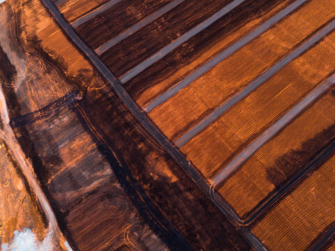 Aerial view of rich terracotta earth meeting dark, charcoal expanses in an industrial tableau of stark contrasts and geometric precision, Aluminium Refinery, Western Australia, Australia.