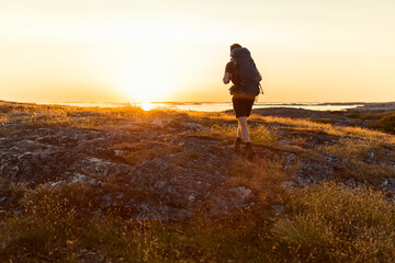 A lone male hiker with a large backpack treks across a rugged, rocky coastal landscape during a golden sunset, overlooking the sea. Perfect for themes of adventure, freedom, and outdoor exploration. © Francis
