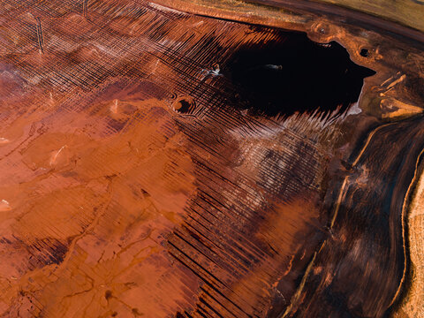 Aerial view of the stark contrast between the dark pool and the red earth, a textured landscape, Aluminium Refinery, Western Australia, Australia.