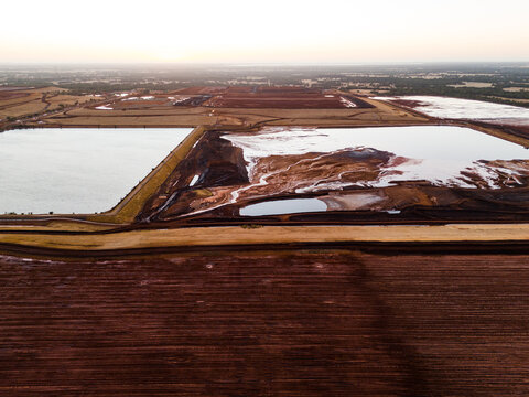 Aerial view of the starkly contrasting red earth meeting the milky waters of the refinery pools under a pale sky, Aluminium Refinery, Western Australia, Australia.