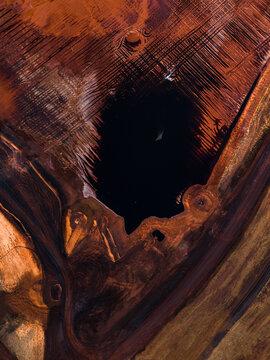 Aerial view of dark void contrasting with the reddish-brown textures, creating an abstract landscape from above, Aluminium Refinery, Western Australia, Australia.