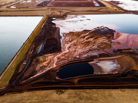 Aerial view of the contrasting textures of the brown earth meet the still waters, creating a stark industrial landscape., Aluminium Refinery, Western Australia, Australia.