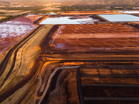 Aerial view of terraced pools reflecting the sky, juxtaposed against the deep red earth, creating a surreal landscape of industry and nature, Aluminium Refinery, Western Australia, Australia.
