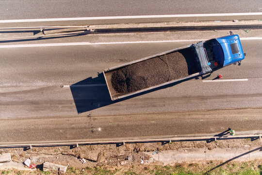Aerial view of a blue car passing a Tack Distributor or bitumen truck while on a soon to be paved roadlane, on highway A-7, Estepona, Andalusia, Spain.