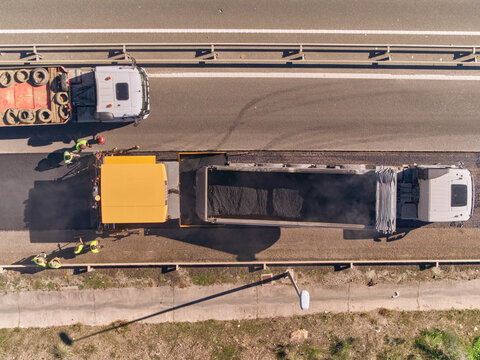 Aerial view of a blue car passing a Tack Distributor or bitumen truck while on a soon to be paved roadlane, on highway A-7, Estepona, Andalusia, Spain.