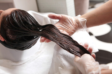 Naklejka premium Long hair is washed and moisturized with a cosmetic mask. Hair care in a beauty salon. Wet hair. The master applies a mask to moisturize the hair.